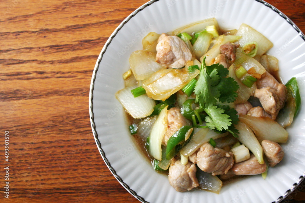 Stir-fried pork with chilli with onions and spring onions served in a white plate, Stir-fried pork with chilli is a popular Thai dish that Thai people eat.
