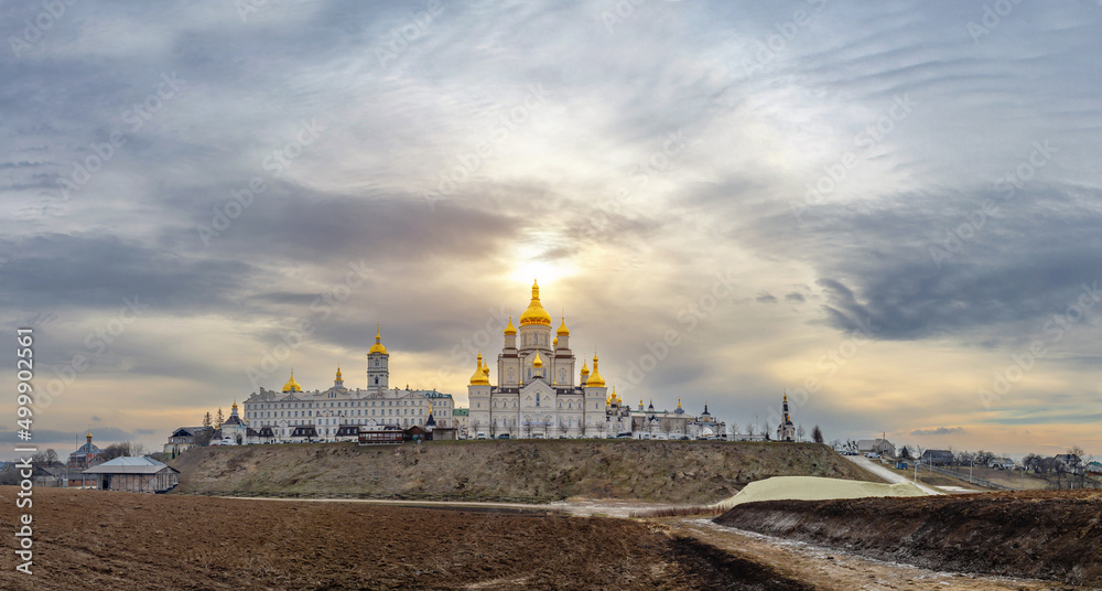 Magical view of the Holy Dormition Pochayiv Lavra in Ukraine. Panoramic view. Sunlight over the monastery. Black clouds are gathering around.