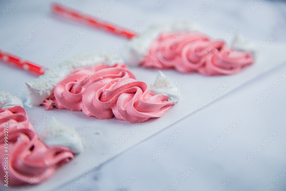 Meringue in the form of pink Christmas hats, with a white bumbone and rim lies on white parchment. High quality photo Meringue in the form of pink Christmas hats, with a white bumbone and rim lies on white parchment. High quality photo
