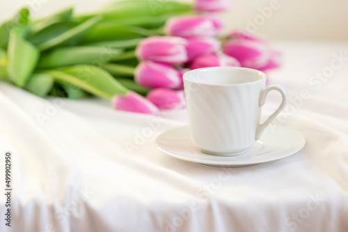 Spring still life with a white mug with a saucer and a bouquet of beautiful pink tulips