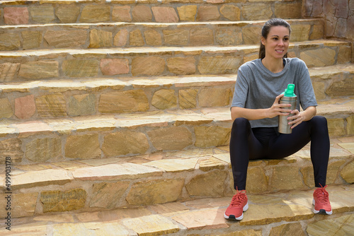 seated sportswoman holding an environmentally friendly aluminum bottle on stairs © Eclipsnet