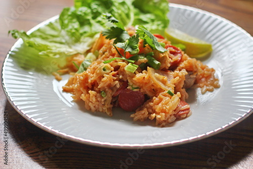 Pork and sausage fried rice served in a plate with lettuce and coriander garnish. Fried rice is a street food that is sold in Thailand.