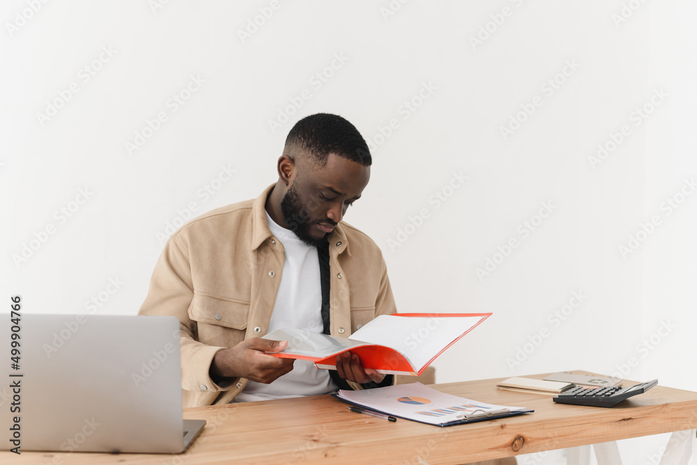 Serious african american man reading notes in business paperwork while sitting at home and working on economic project Serious african american man reading notes in business paperwork while sitting at home and working on economic project