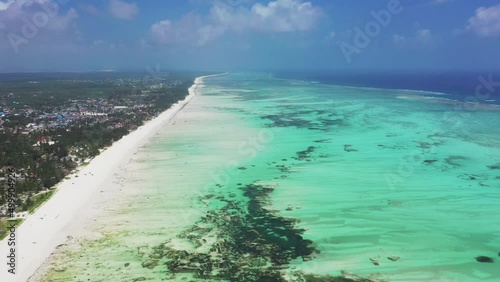 High forward-moving drone aerial view of Paje village, the beach and its blue lagoon, and the coral reef, with people kitesurfing