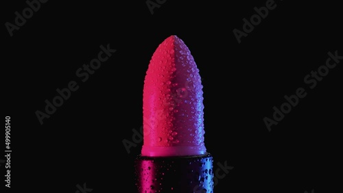 A tube of red female lipstick in raindrops rotates on a black background. Macro shooting. photo