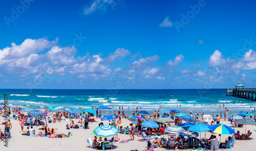 umbrellas on beach with people relaxing. tourist visiting Florida. clouds in sky over sea 