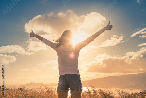 Happiness and freedom concept. Woman with thumbs up facing the sunrise. 