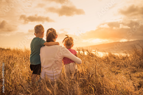 Mother and children sitting in meadow watching the golden sunset. Family adventure 