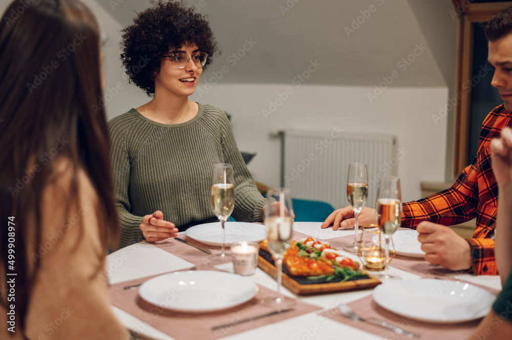 Group of friends enjoying dinner while sitting at the kitchen table together Group of friends enjoying dinner while sitting at the kitchen table together
