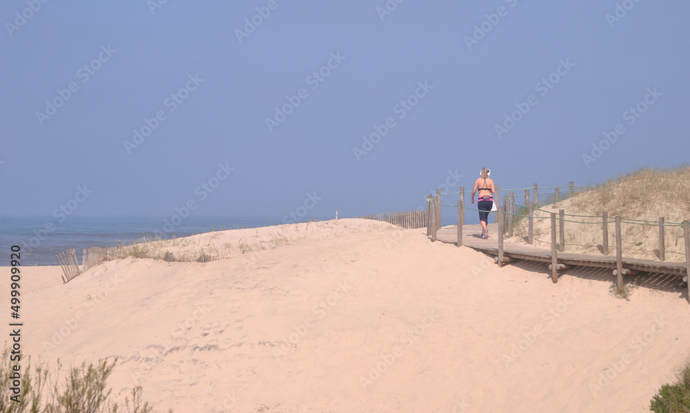 Mulher a caminhar num passadiço á beira mar, duna de uma praia