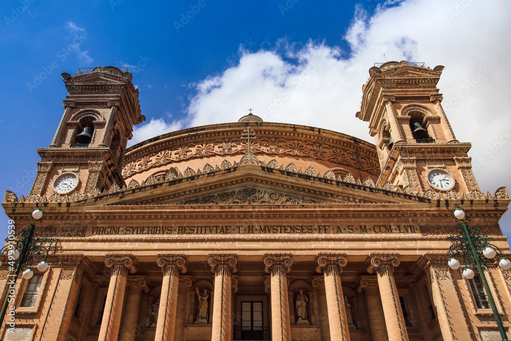 Malta island Mosta Rotunda, the Sanctuary Basilica of the Assumption of Our Lady - Santwarju Bazilika ta Santa Marija, 17th century Catholic church facade against blue sky with clouds.