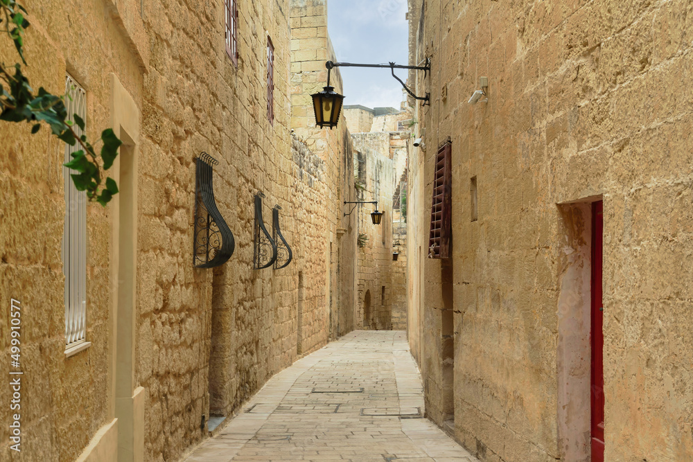 Mdina, Malta empty narrow alley along traditional stone built houses in the medieval historic Silent city paved with stone slabs and yellow limestone walls with vintage shape hanging lanterns.