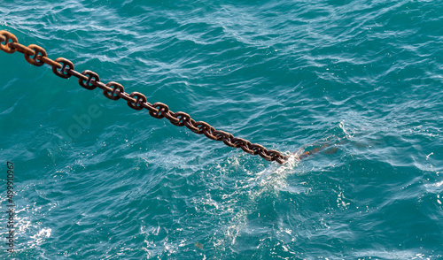 Anchor chain going dowm in the water with waves and splashes.