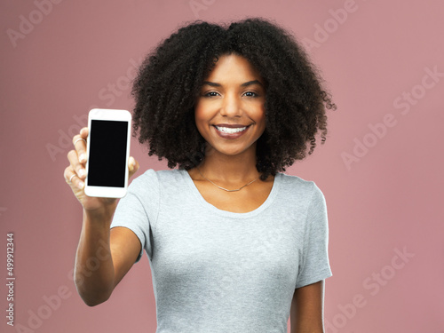 I downloaded mine, now to get yours. Studio shot of an attractive young woman holding a smartphone with a blank screen against a pink background.