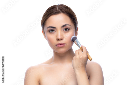 Close up portrait of a beautiful half naked woman with perfect, natural, clean and cosmetic skin and looking ahead. Hold makeup brush, make up in process. Isolated over white background.
