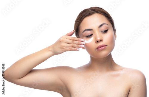 Close up portrait of a beautiful half naked woman with perfect, natural, clean and cosmetic skin. Applying cosmetic skincare cream, hydrated, lotion or mask on her face. Isolated over white background