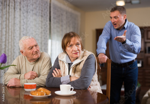 Adult annoyed man scolding his senior parents at home