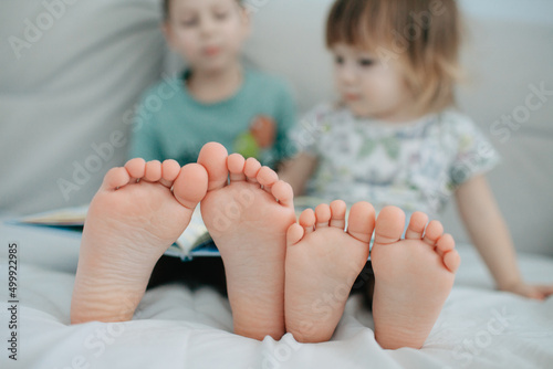 Big brother and little sister holding bare feet close up to camera . Blurred face on background
