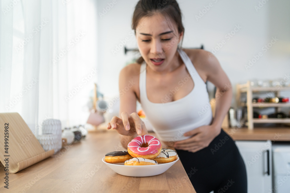 Asian beautiful young woman hungry and want to eat donut in kitchen. 
