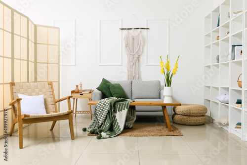 Interior of stylish living room with comfortable sofa and gladiolus flowers