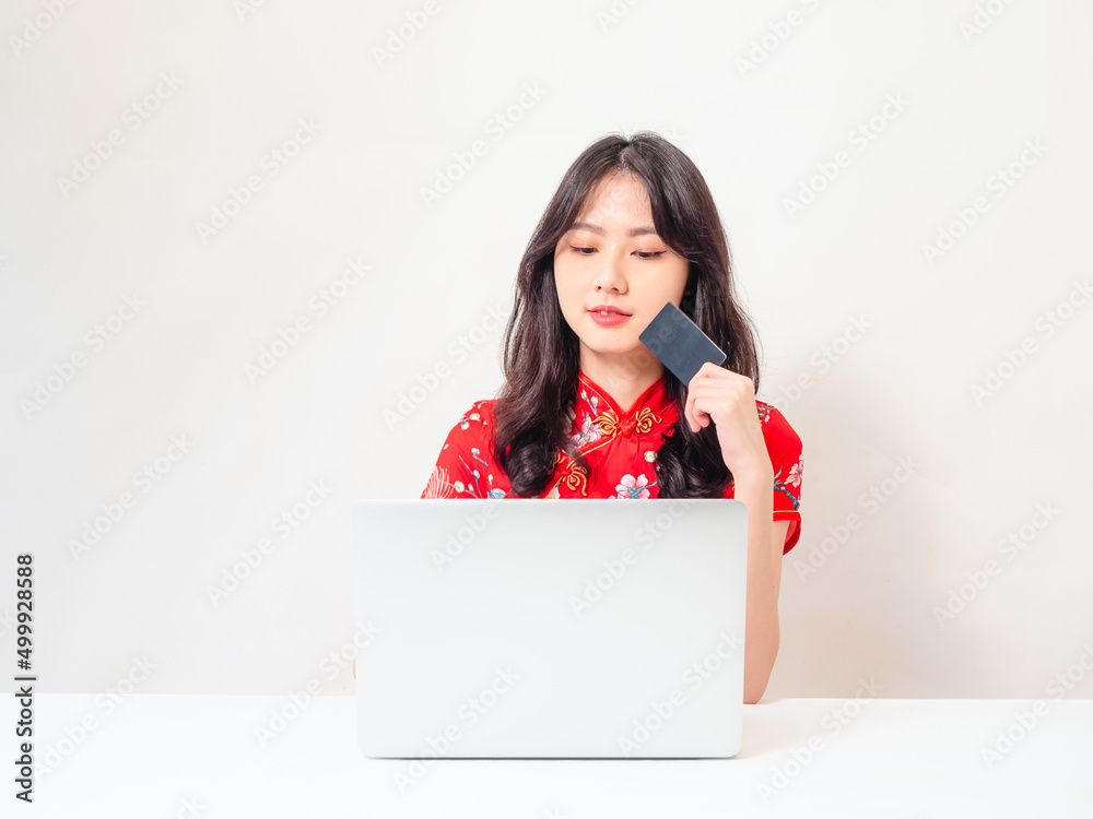 Asian young woman wearing traditional cheongsam qipao dress using laptop and credit card shopping online, e-commerce concept isolated on white background.