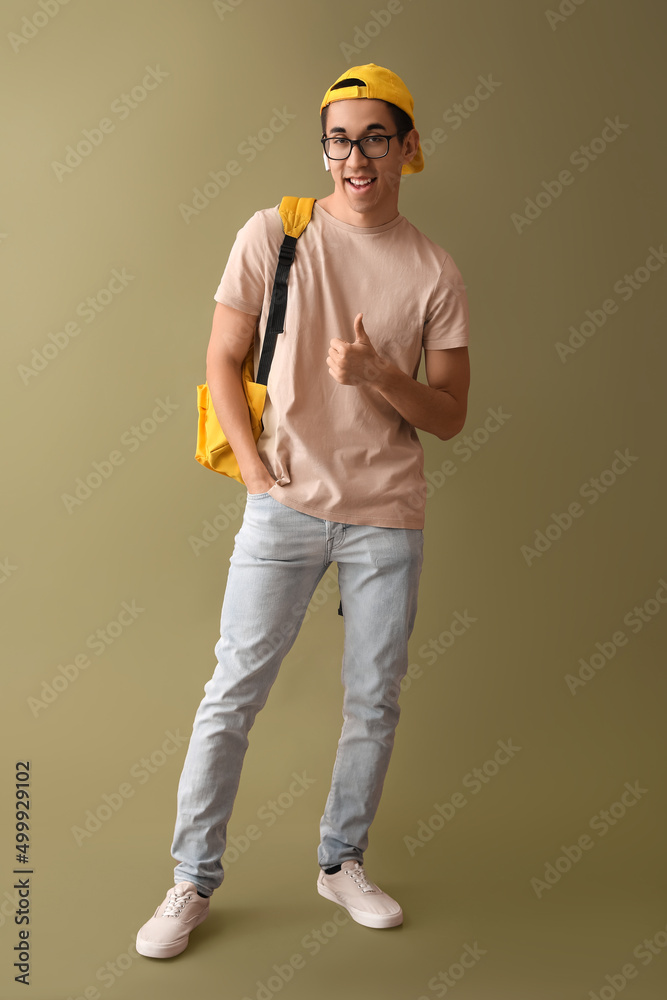 Male Asian student in eyeglasses showing thumb-up on color background