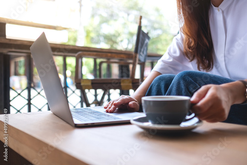 Closeup image of a woman working and typing on laptop computer while drinking coffee