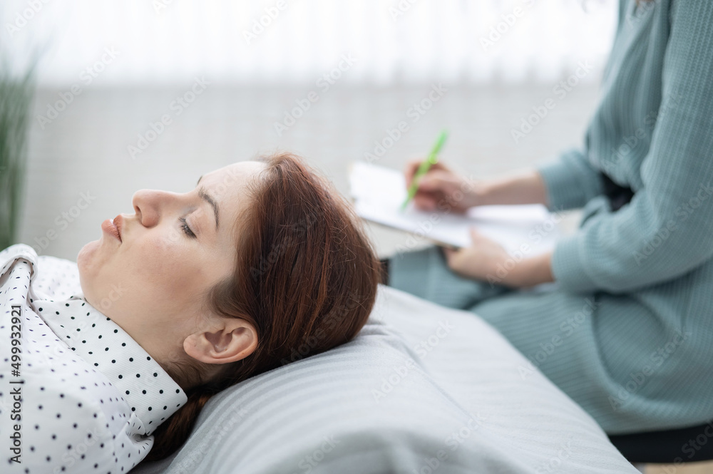 A caucasian woman lies on a couch and expresses her feelings, while a psychologist makes notes on a tablet. A caucasian woman lies on a couch and expresses her feelings, while a psychologist makes notes on a tablet.
