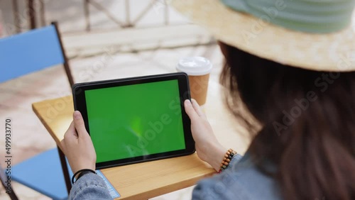 Technology concept. Close up. Caucasian Girl using device. Young female in hat tapping on tabley green screen. Beautiful woman view photos and videos on tablet device. Over shoulder green screen view.