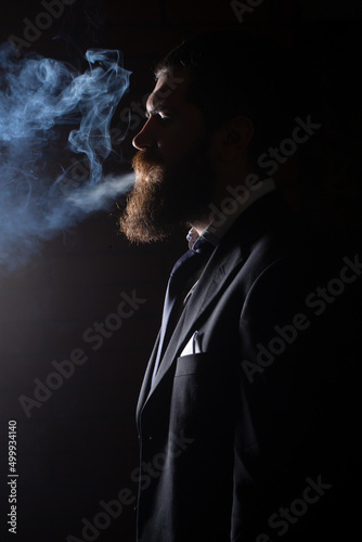 Cigarette smoke on black background. Businessman in suit smoking cigarette.