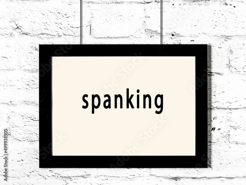 Black frame hanging on white brick wall with inscription spanking