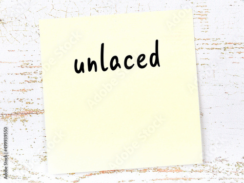 Yellow sticky note on wooden wall with handwritten word unlaced photo