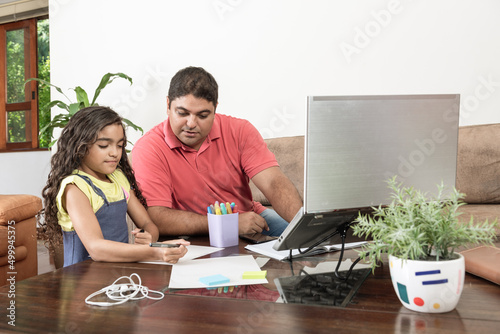 Pai trabalhando com filha fazendo dever de casa na sala de estar photo