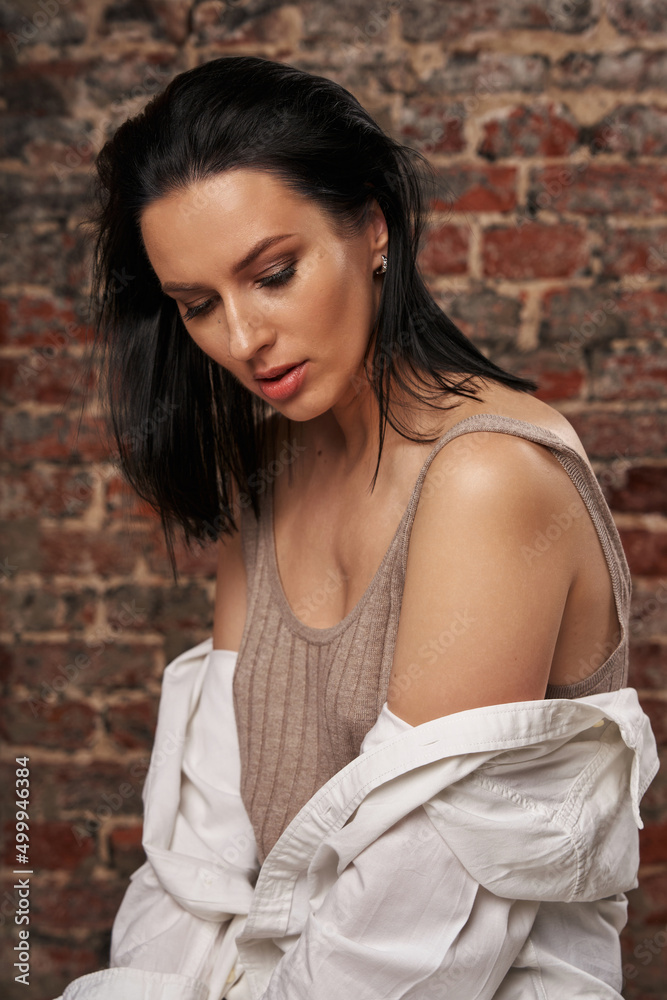 a beautiful woman with dark hair lowered her head, a white shirt fell from her shoulder