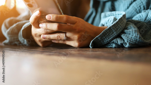 A woman s hand is typing text messages  chatting via apps  or searching for information on a smartphone on a wooden table in a restaurant or caf   on weekends.