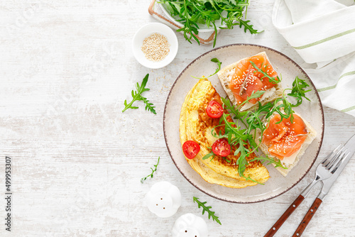 Omelette or omelet, fresh arugula and tomato salad and toasts with butter and salted salmon, top view