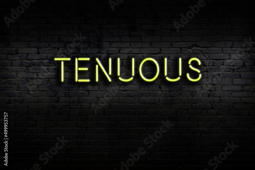 Neon sign. Word tenuous against brick wall. Night view