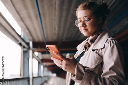 young caucasian female student, generation z, dressed in a trench coat in the parking lot uses a smartphone