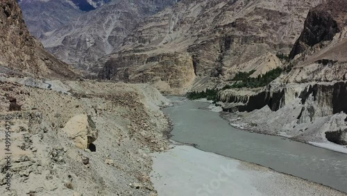 aerial drone flying over a mountain cliff towards the fast flowing gray Indus River in Skardu Pakistan overlooking the large mountains during a sunny summer day photo