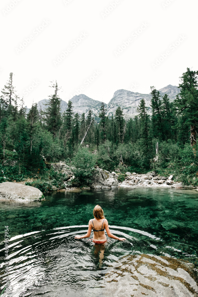 Girl in swimming suite with the back at the camera swimming in a beautiful mountain lake, surrounded pine forest