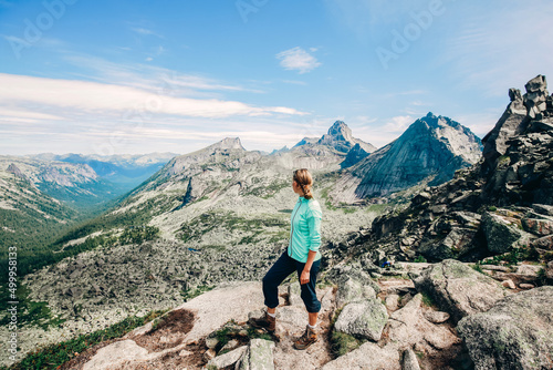 Girl on mountain peak with looking at beautiful mountain valley. Landscape with sporty young woman, blue sky and sunny day. Travel and tourism. Hiking © Margarita Timofeeva