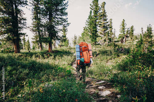 Man hiker on summer day and with big heavy hiking backpack full of travel staff. Travel Lifestyle concept adventure summer vacations outdoor wild landscape on background. 