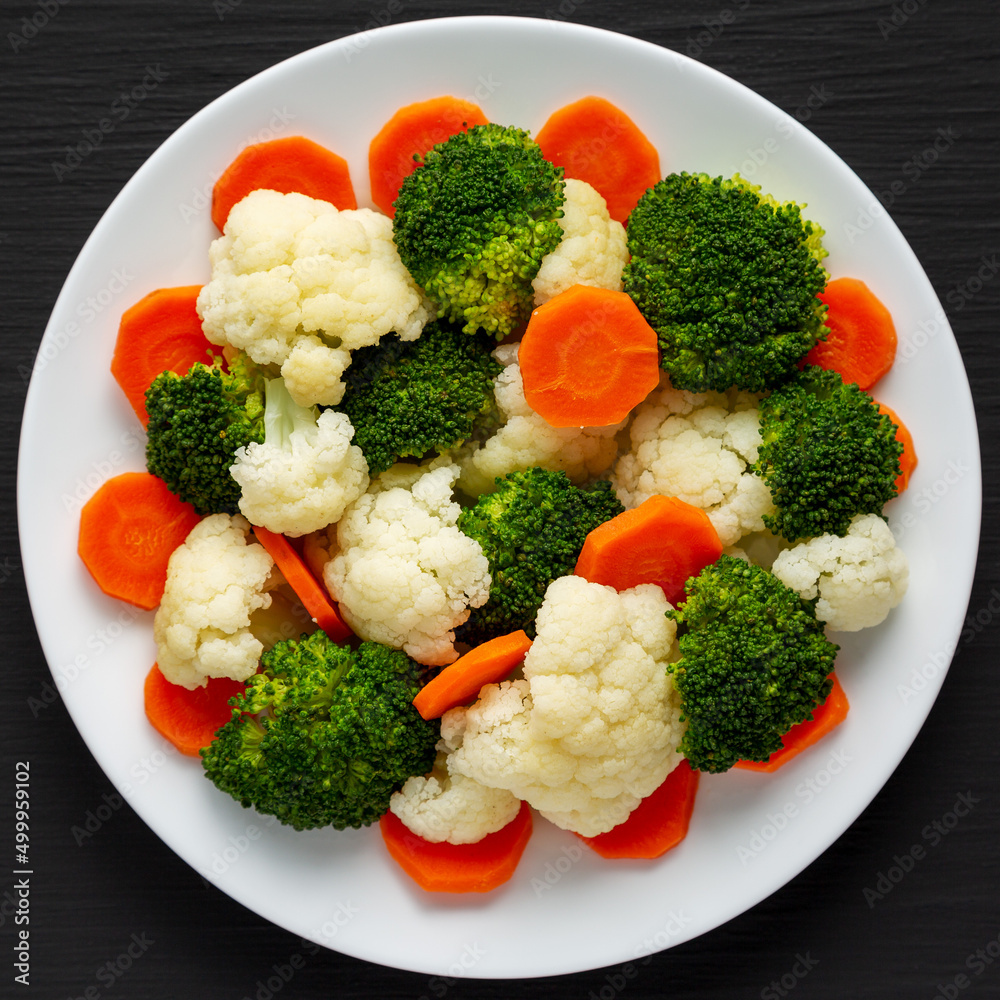 Mixed Organic Steamed Vegetables (Carrots, Broccoli and Cauliflower) on a Plate on a black background, top view. Flat lay, overhead, from above. Mixed Organic Steamed Vegetables (Carrots, Broccoli and Cauliflower) on a Plate on a black background, top view. Flat lay, overhead, from above.