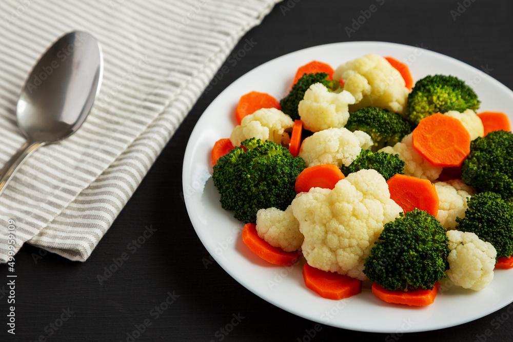 Mixed Organic Steamed Vegetables (Carrots, Broccoli and Cauliflower) on a Plate on a black surface, side view. Mixed Organic Steamed Vegetables (Carrots, Broccoli and Cauliflower) on a Plate on a black surface, side view.