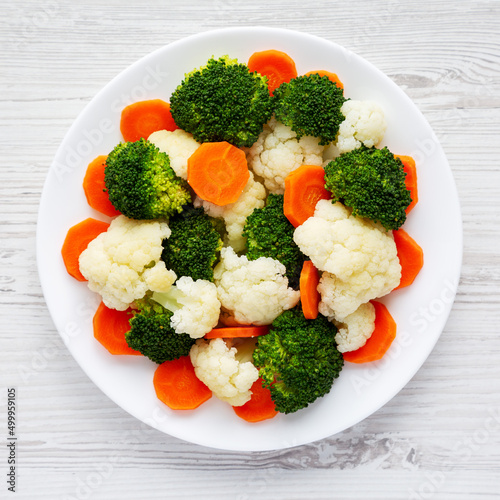 Mixed Organic Steamed Vegetables (Carrots, Broccoli and Cauliflower) on a Plate on a white wooden background, top view. Flat lay, overhead, from above.