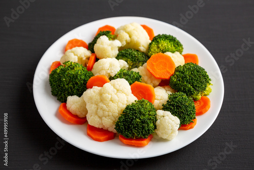 Mixed Organic Steamed Vegetables (Carrots, Broccoli and Cauliflower) on a Plate on a black background, low angle view.