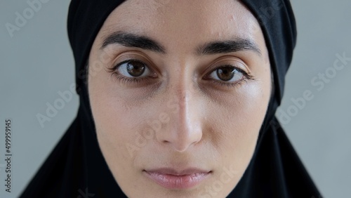 An Arab woman. The head is covered with a black hijab. The hijab hides her hair beauty. The face is oval, the eyebrows are thick black, the woman has large almond-shaped eyes.