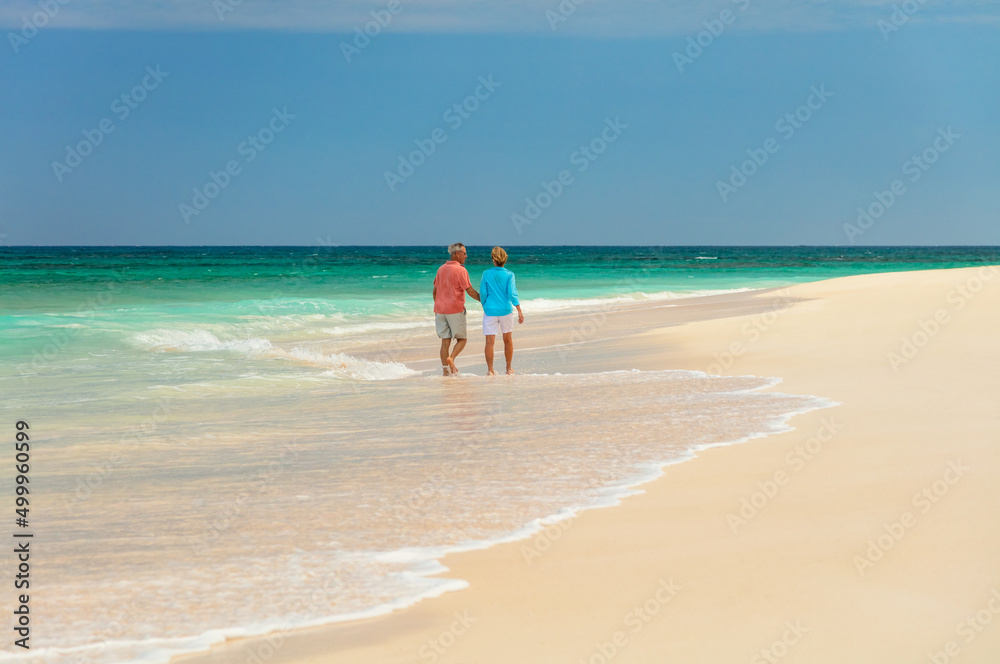 Loving senior couple walking on white sandy beach Loving senior couple walking on white sandy beach
