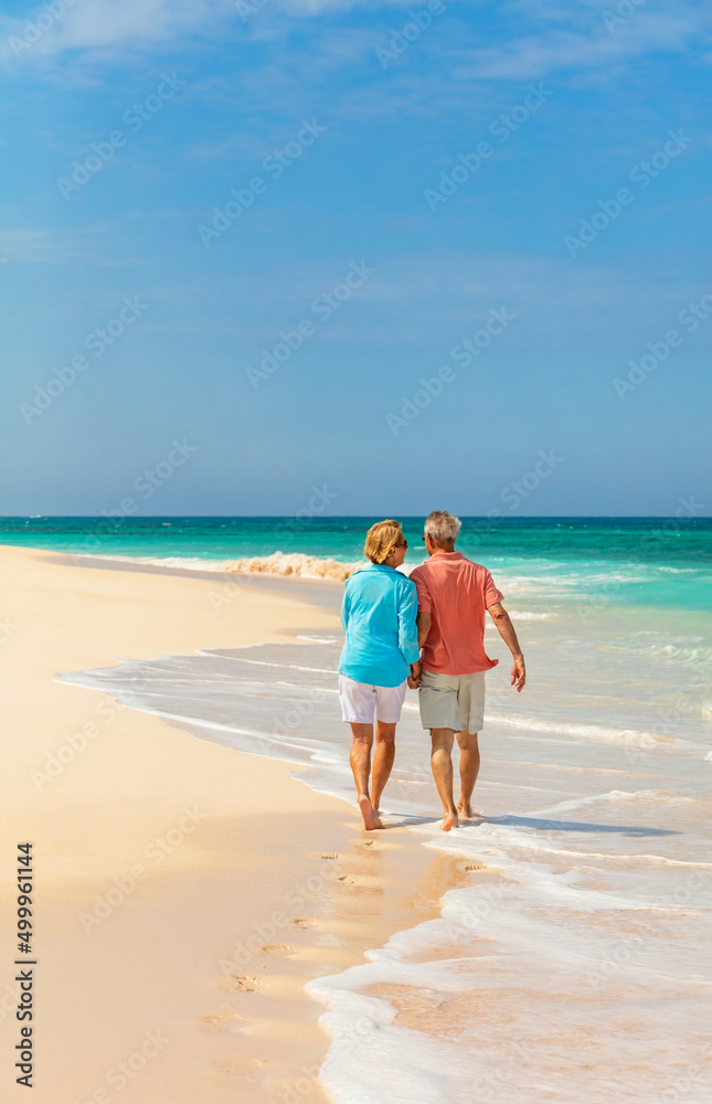 Travel retired couple walking barefoot on tropical beach