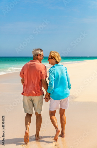 Loving mature couple walking barefoot on tropical beach